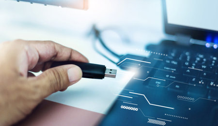 Close-up shot, hand holding of USB being connected to laptop computer with graphic symbol that data...