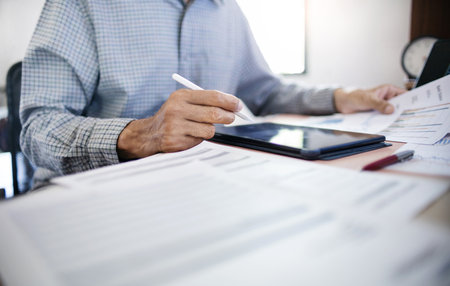 Businessman in office using tablet with documents and chart for analyzing data of investment to make investment plan for a future, financial investment concept.の写真素材