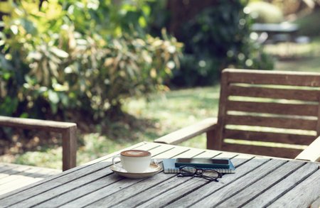 Latte coffee with mobile and note book on old wooden table in outdoor garden