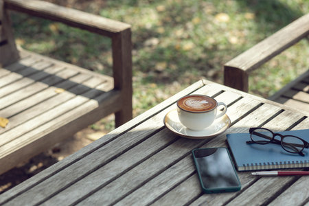 Latte coffee with mobile and note book on old wooden table in outdoor garden