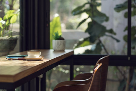 White coffee cup with mobile and note book on wooden counter with seat in cafe and outdoor garden backgroundの写真素材
