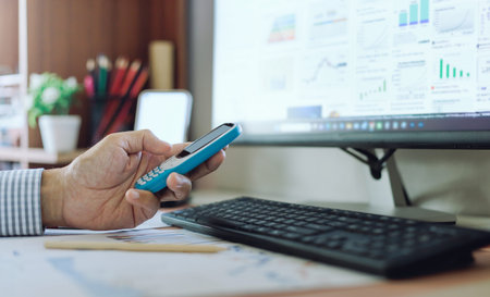 Hand of businessman use old mobile phone to contact an investment advisor. use desktop PC searching...