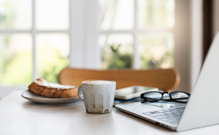 Comfortable workplace with laptop computer, eyeglasses with coffee cup and breakfastの写真素材