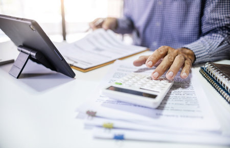 Asian businessman using a calculator to calculate expenses, taxes, financial documents and analyzing business data to plan for future business growthの写真素材