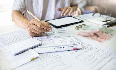 Asian man review business loan application and checking bank statement online via tablet before apply for loan approval to start new businessの写真素材