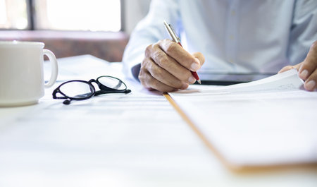 Asian businessman reviewing document reports at office workplace. legal expert, professional lawyer reading and checking financial documents or insurance contract befor signの写真素材
