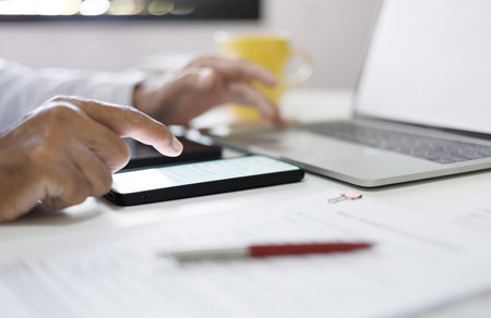 Asian man using smart phone checking document and working with laptop computer at home to start new business online, close up shotの写真素材