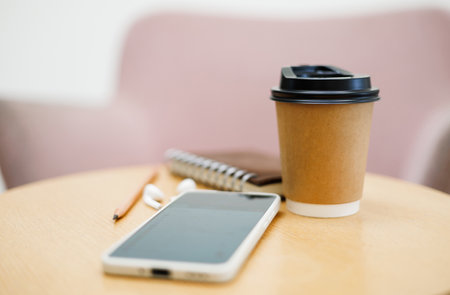 Close up shot, take away coffee cup with smartphone, notebook and pencil on wooden tableの写真素材