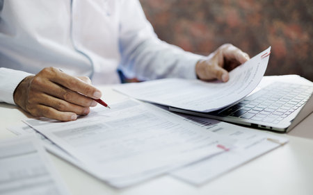 asian businessman holding pen reviewing document and business contract on desk in office using computer laptop working and meeting onlineの写真素材