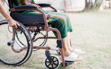 cropped shot, middle age female on wheelchair and hand grip on wheel on grass field at home she resting after being sickの写真素材