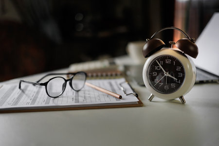 alarm clock on table near laptop, documents and eyeglasses. time management concept, routine work, education, office workplace, planningの写真素材