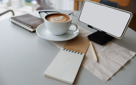 smart phone on stand with latte coffee, note book and diary on tableの写真素材