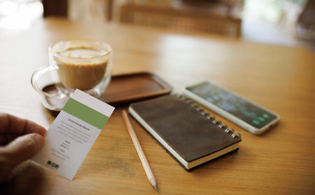 close up shot, man hand holding name card with smart phone, notebook and coffee drink on wooden tableの写真素材