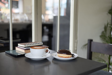 coffee cup with latte coffee and mobile phone, book for read, diary for taking note and donut on black tableの写真素材