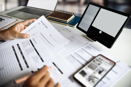 Businessman analyzing documents with laptop and smartphone.