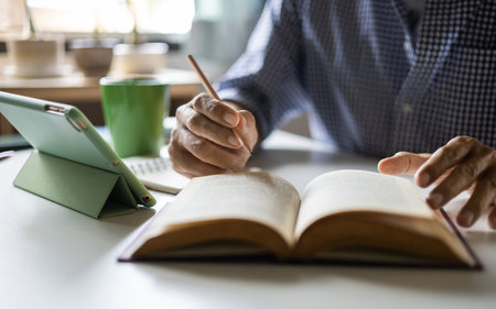 close up shot, asian man reading book and using digital tablet to seek knowledge, study and working onlineの写真素材