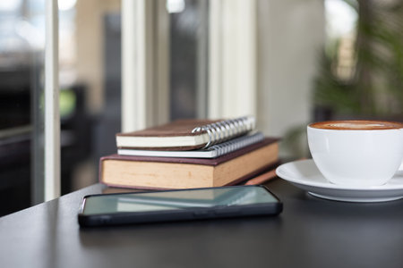coffee cup with latte coffee and mobile phone, book for read, diary for taking note on black tableの写真素材