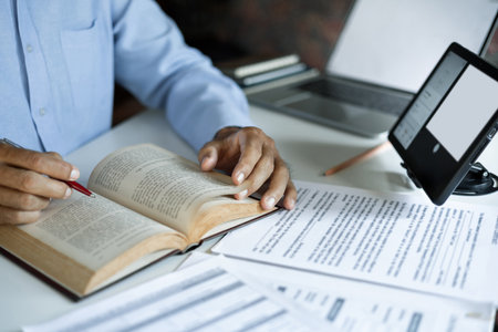 asian man reading book using tablet and laptop with documents working and learning online to Increasing knowledge via internet technology, close up shotの写真素材