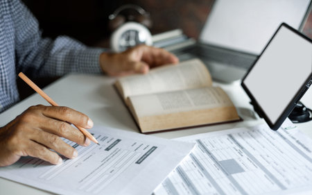 asian man checking business document find knowledge in book using tablet and laptop to working...