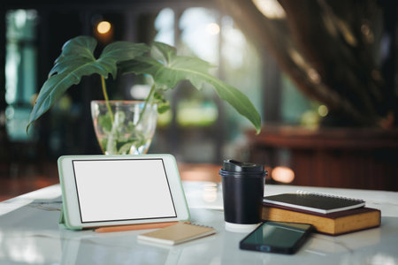 Close up shot, blank screen tablet with coffee cup, glass vase with leaf and other items for working on table, outdoor workplace with sunlightの写真素材