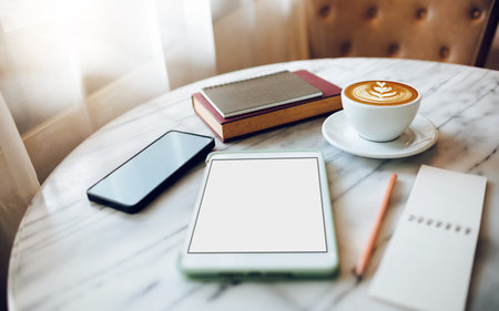 close-up view, blank screen on tablet with coffee drink, mobile phone and note pad on table in cafe...