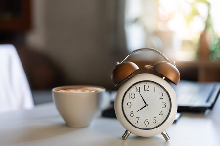 close up shot, alarm clock at 8 AM. with coffee drink and laptop on desk. work or study in the...