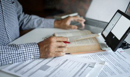 asian man reading book using tablet and laptop with documents working and learning online to...