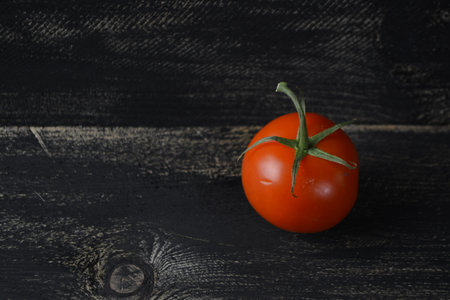 Red tomato on a black wooden background, close-up with a place for textの写真素材