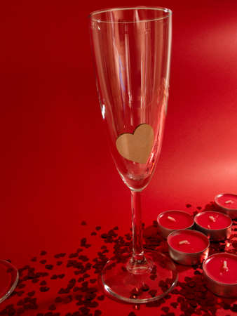 Glasses of champagne, red candles, red confetti in the shape of a heart on a red backgroundの写真素材