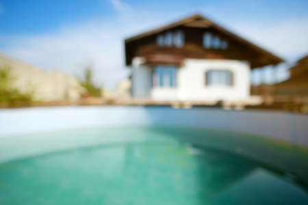 Blurred abstract background of house at the summer. House exterior theme creative abstract blur background with bokeh effect. Blurred house, lawn, poolの写真素材