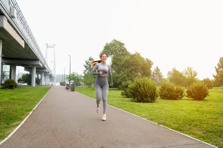 Woman dressed leggings and top running asphalt road summer park. Healthy lifestyle concept. Active...
