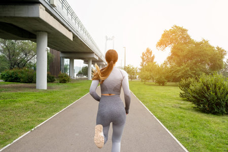 Woman dressed leggings and top running asphalt road summer park. Healthy lifestyle concept. Active...