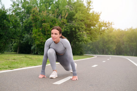 Woman dressed leggings and top running asphalt road summer park. Healthy lifestyle concept. Active and athletic female exercises oundoorの写真素材