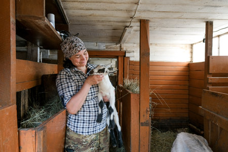 Female farmer snuggling baby goat in hands. Cute baby goat portraitの写真素材