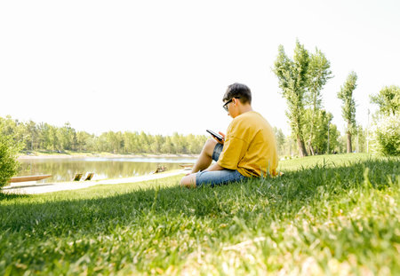 Happy young guy sit grass, enjoy a sunny day at park with cup of coffee. Outdoor picnic launch time....