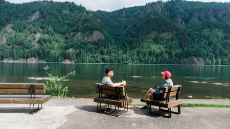 man and woman sit back on bench enjoying valley landscape view from top of a mountain. adult tourists couple sitting in the bench. Panoramic view of mountain hills, Carpathian mountainsの写真素材