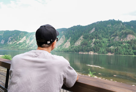 Back view of male traveler sitting on wooden bench while enjoying amazing nature in mountains. Man drinking coffee outdoors in the morning.の写真素材