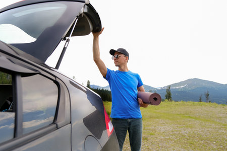 Men standing near car with open trunk planning to do yoga on mat. Outdoor yoga in mountains