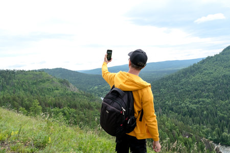 man with backpack taking selfie with mobile smart phone hiking mountains. Tourist looking at mountain beauty landscape from the top of hill.の写真素材