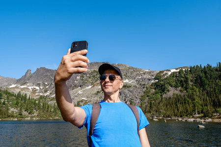 Traveling man using phone to take a photoes in mountain landscape. Blogger takes a selfie