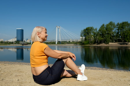 Back view of Senior woman looking lake on a beach. Concept of healthy active life outdoor. Female near the public pond in a city.の写真素材