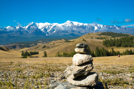 Scenic view from sunlight grassy hill with road to high mountain range. Beautiful sunny mountain landscape with large snow peak mountains. Road trip to Altai.の写真素材
