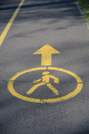 yellow pedestrian path sign on asphalt in park