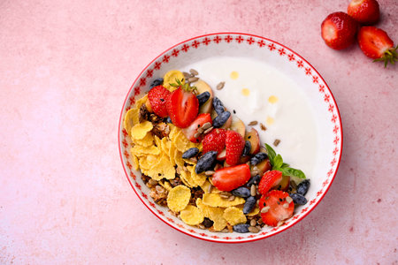 Plate with yogurt and muesli topped with fresh strawberries on pink background. Summer breakfast...