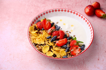 Plate with yogurt and muesli topped with fresh strawberries on pink background. Summer breakfast...