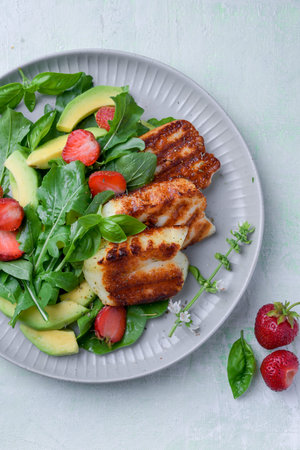 Plate of summer salad with fresh strawberries, arugula, and grilled halloumi cheese. Bright, flavorful, and healthy dish perfect for warm seasons.の写真素材