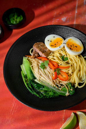 Top view of ramen in black bowl. Traditional Japanese noodle soup with rich broth, vegetables, and...