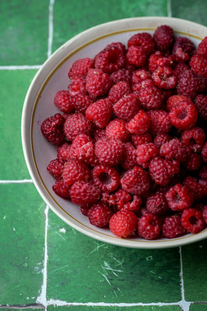 Plate of freshly picked red raspberries on green tile background. Concept of vibrant colors, summer,...