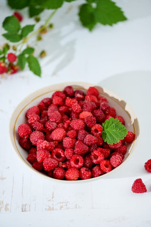 Plate of freshly picked raspberries on white wooden background. Concept of harvest, healthy organic...