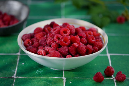 Plate of freshly picked red raspberries on green tile background. Concept of vibrant colors, summer,...
